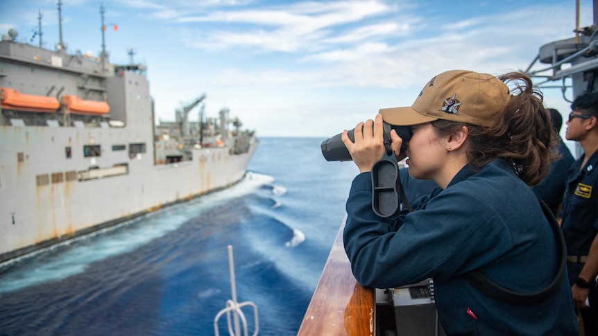 Seorang perwira angkatan laut melihat kapal lain melalui pengintai.