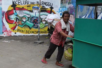Seorang pria berjalan melewati mural yang mendorong warga untuk bangkit melawan COVID-19 di desa Bidara Sena, Kecamatan Jatingara, Jakarta Timur, Sabtu, 1 Januari 2022 (Foto: Kuncoro Widyo Rumpoko/Pacific Press/Sipa USA via Reuters)
