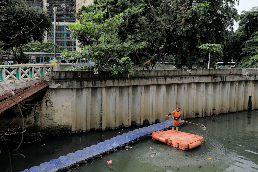 Seorang pekerja kota yang mengenakan pakaian oranye membersihkan kanal yang tercemar di Jakarta