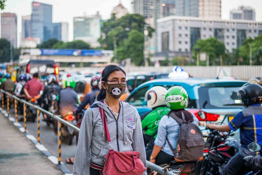 Seorang wanita berjalan di jalan Jakarta mengenakan topeng