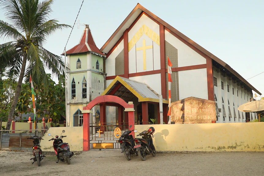 Sebuah gereja berubin putih dengan sepeda motor duduk di depan gerbang.